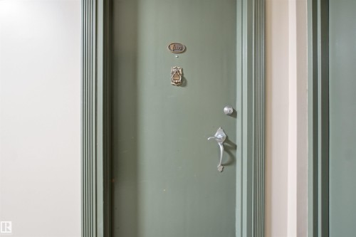 Sage green door with an ornamental door knocker, silver-toned doorknob, and decorative door handle - #1115 13910 Stony Plain Rd Nw, Edmonton, AB 