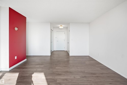 Spacious room with wood-finish flooring, white walls, and a distinctive red accent wall - #1115 13910 Stony Plain Rd Nw, Edmonton, AB 