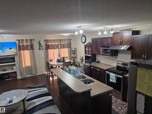 Kitchen featuring dark wood-finish cabinetry, stainless steel appliances, and a double basin sink - 1474 33B Street Nw, Edmonton, AB 