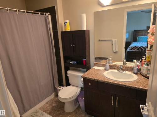 Dark wood-finish vanity with a built-in sink, stone-finish countertop, and wall-mounted mirror - 1474 33B Street Nw, Edmonton, AB 