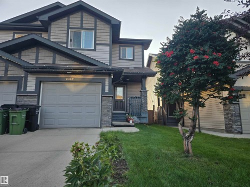 Exterior featuring a stone and siding facade, attached garage, front entryway, and a mature tree with red berries - 1474 33B Street Nw, Edmonton, AB 