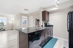 Kitchen island with an undermount sink, dark cabinetry, black refrigerator, and light wood-finish flooring - 