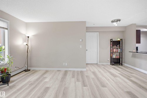 Light wood-finish flooring throughout, bright window, neutral painted walls, and a white paneled door - #212 12035 22 Av Sw, Edmonton, AB 