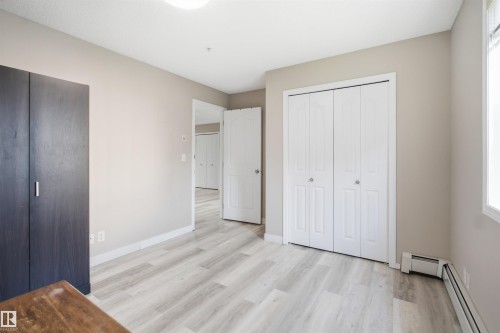 Light wood-finish flooring, neutral wall paint, white bi-fold closet doors, and white trim - #212 12035 22 Av Sw, Edmonton, AB 