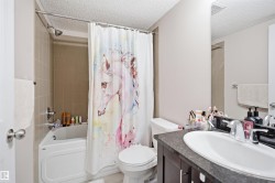 Bathroom featuring a shower-tub combination with light-toned wall tiling, dark-toned vanity with an integrated sink, and an expansive wall-mounted mirror - 