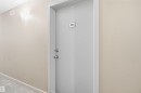 Interior entry door with brushed nickel hardware, wall-mounted sconce, and neutral wall paint - #212 12035 22 Av Sw, Edmonton, AB 