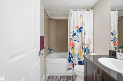 White panel door, tub-shower combination with tiled surround, dark wood-finish vanity with an undermount sink and dark countertop, and a wall-mounted mirror - 