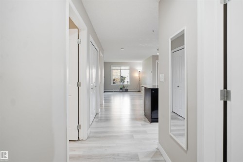 Hallway featuring wood-finish flooring, light gray wall paint, white trim, and white paneled doors - #212 12035 22 Av Sw, Edmonton, AB 