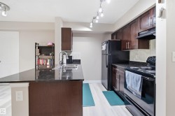 Kitchen featuring a dark stone countertop, dark wood-finish cabinetry, black appliances, and light wood-finish flooring - 