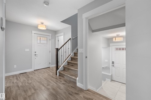 Wood-finish flooring, staircase with dark wood-finish handrail and black spindles, white interior doors, and flush mount lighting - 2585 Pegasus Boulevard Nw, Edmonton, AB 