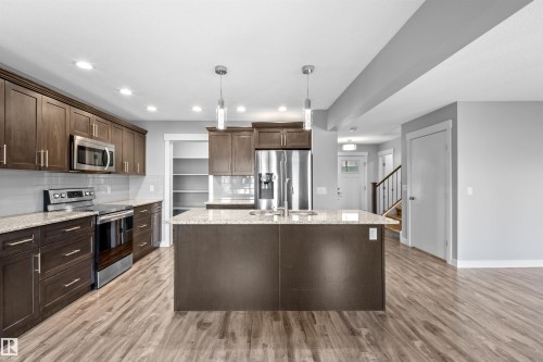 Kitchen featuring a central island, wood-finish flooring, dark wood cabinetry, light-toned countertops, and stainless steel appliances - 2585 Pegasus Boulevard Nw, Edmonton, AB 