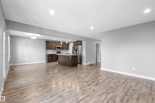 Open-concept layout with wood-finish flooring, recessed lighting, and a kitchen featuring dark wood cabinetry, a central island, and stainless steel appliances - 2585 Pegasus Boulevard Nw, Edmonton, AB 