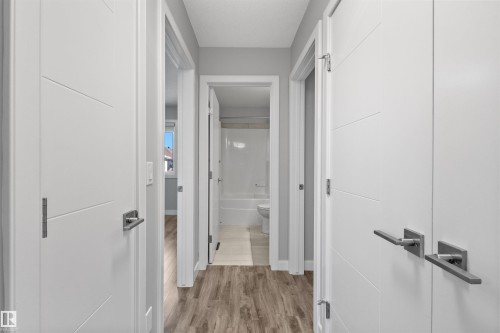 Hallway featuring wood-finish flooring and modern white doors with horizontal paneling and brushed nickel hardware - 2585 Pegasus Boulevard Nw, Edmonton, AB 