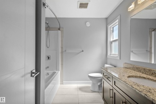 Full bathroom featuring a single-basin vanity with a granite countertop and dark wood-finish cabinetry, a toilet, and a combined shower and bathtub with a curved shower rod - 2585 Pegasus Boulevard Nw, Edmonton, AB 