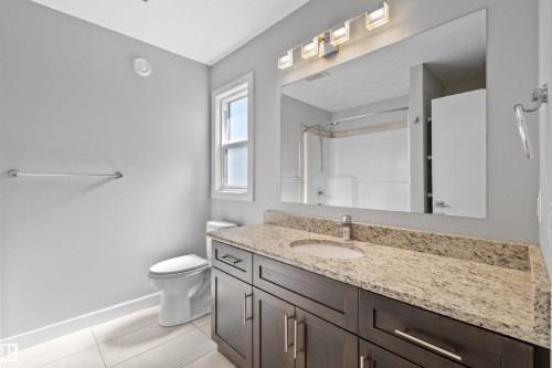 Dark wood-finish vanity with an undermount sink, speckled countertop, and large wall-mounted mirror - 2585 Pegasus Boulevard Nw, Edmonton, AB 
