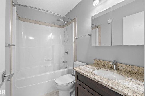 Bathroom with a white tub and shower combination, dark wood-finish vanity with an undermount sink, speckled countertop, and a mirrored medicine cabinet - 2585 Pegasus Boulevard Nw, Edmonton, AB 