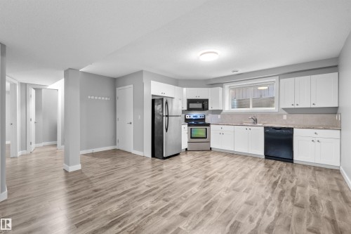 Open-concept kitchen and living area featuring wood-finish flooring, white cabinetry, stainless steel refrigerator and range, and a black dishwasher - 2585 Pegasus Boulevard Nw, Edmonton, AB 