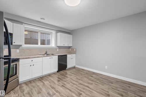 Kitchen area featuring white cabinetry, stainless steel appliances, wood-finish flooring, and a window with a stone-finish backsplash - 2585 Pegasus Boulevard Nw, Edmonton, AB 