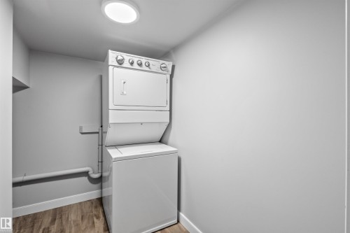 Dedicated laundry area featuring a white stackable washer and dryer, wood-finish flooring, and a flush mount ceiling light - 2585 Pegasus Boulevard Nw, Edmonton, AB 