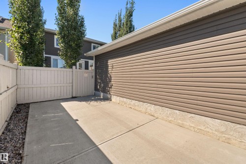 Concrete pad with gravel border, alongside a light-colored privacy fence with gate, and building with horizontal siding - 2585 Pegasus Boulevard Nw, Edmonton, AB 
