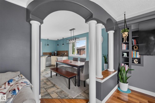 Archway opening with decorative columns, built-in shelving, wood-finish flooring, and a kitchen beyond featuring a window and pendant lighting - 131 Pine Drive, Wetaskiwin, AB - Indoor