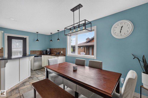 Dining area featuring a dark wood-finish table with a linear pendant light fixture above, tile flooring, a window offering exterior views, and a kitchen bar with a black countertop - 131 Pine Drive, Wetaskiwin, AB - Indoor Photo Showing Dining Room