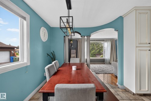 Dining area featuring a wood-finish table, a contemporary linear chandelier, tiled flooring, and an arched entryway with decorative columns - 131 Pine Drive, Wetaskiwin, AB - Indoor Photo Showing Dining Room