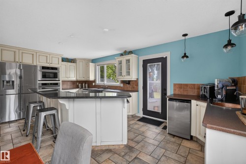 Spacious kitchen featuring an expansive center island with seating, stainless steel appliances, ample cream cabinetry, a tiled backsplash, and stone-finish flooring - 131 Pine Drive, Wetaskiwin, AB - Indoor Photo Showing Kitchen
