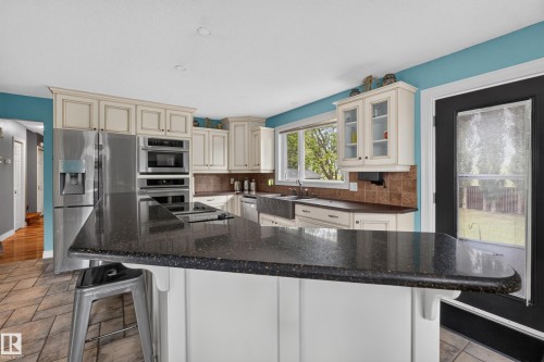 Kitchen featuring an expansive dark stone countertop island, cream-colored cabinetry, stainless steel appliances, and tile flooring - 131 Pine Drive, Wetaskiwin, AB - Indoor Photo Showing Kitchen