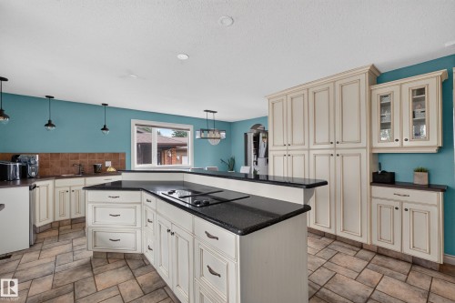 Expansive kitchen featuring an angled island with a built-in cooktop, dark speckled countertops, and an abundance of cream-colored cabinetry with dark hardware - 131 Pine Drive, Wetaskiwin, AB - Indoor Photo Showing Kitchen