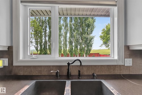 Dual-basin sink with an oil-rubbed bronze faucet set against a tiled backsplash and solid surface countertop - 131 Pine Drive, Wetaskiwin, AB - Indoor Photo Showing Kitchen With Double Sink