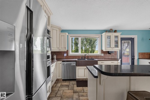 Kitchen featuring stainless steel appliances, off-white cabinetry with dark hardware, a farmhouse-style sink, solid surface countertops, and tiled flooring - 131 Pine Drive, Wetaskiwin, AB - Indoor Photo Showing Kitchen With Double Sink