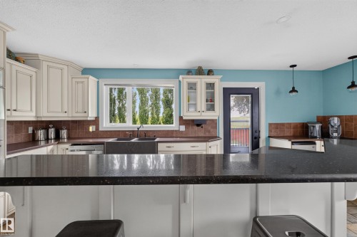 Kitchen featuring dark countertops, cream cabinetry, and a tile backsplash - 131 Pine Drive, Wetaskiwin, AB - Indoor Photo Showing Kitchen With Double Sink