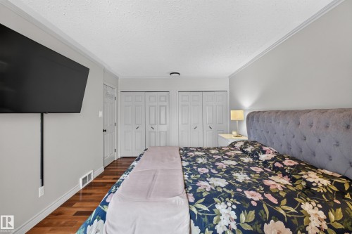 Bedroom featuring wood-finish flooring, two sets of bi-fold closet doors, crown molding, and light gray wall paint - 131 Pine Drive, Wetaskiwin, AB - Indoor Photo Showing Bedroom