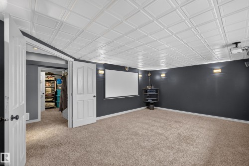 Carpeted room with a projector screen, white coffered ceiling, and dark accent wall - 131 Pine Drive, Wetaskiwin, AB - Indoor