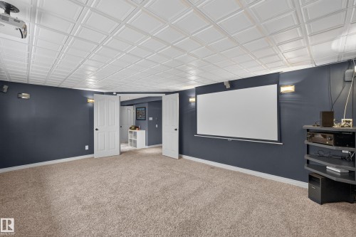 Carpeted room featuring a projector screen, white acoustical tile ceiling, recessed lighting, and double panel doors - 131 Pine Drive, Wetaskiwin, AB - Indoor Photo Showing Other Room