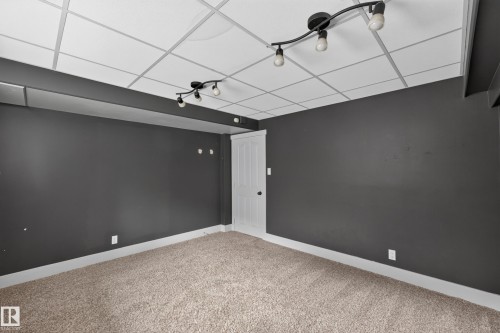 Carpeted room featuring dark walls, white trim, and a drop ceiling with track lighting - 131 Pine Drive, Wetaskiwin, AB - Indoor Photo Showing Other Room