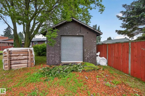 Detached storage shed with a roll-up door, set on a sloped grassy terrain with red bark accents - 131 Pine Drive, Wetaskiwin, AB - Outdoor