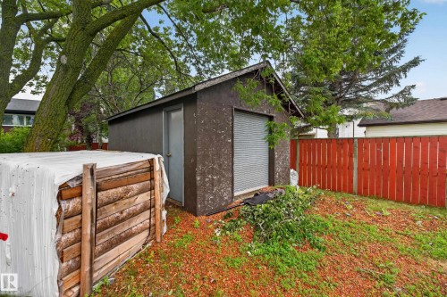 Detached utility shed featuring a roll-up door and separate entry door, bordered by a vibrant red wooden fence - 131 Pine Drive, Wetaskiwin, AB - Outdoor With Exterior