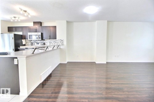 Kitchen featuring dark wood-finish cabinetry, stainless steel appliances, and a mosaic tile backsplash - #18 4850 Terwillegar Cm Nw, Edmonton, AB 