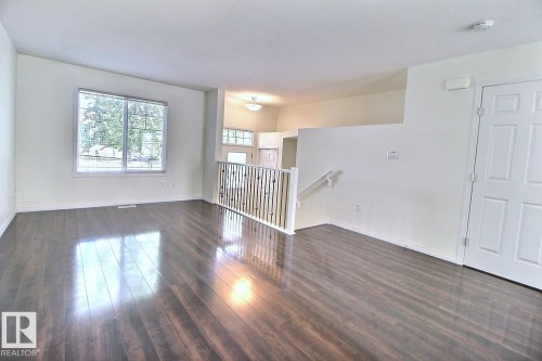 Spacious interior featuring wood-finish flooring, a large window with blinds, and white interior doors - #18 4850 Terwillegar Cm Nw, Edmonton, AB 