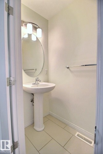 Pedestal sink with chrome faucet, oval mirror, and contemporary vanity lighting - #18 4850 Terwillegar Cm Nw, Edmonton, AB 