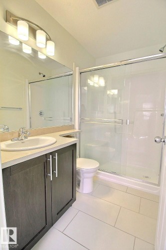 Bathroom with a single vanity, a built-in mirror, a walk-in shower with a glass enclosure, and light-toned rectangular floor tiles - #18 4850 Terwillegar Cm Nw, Edmonton, AB 