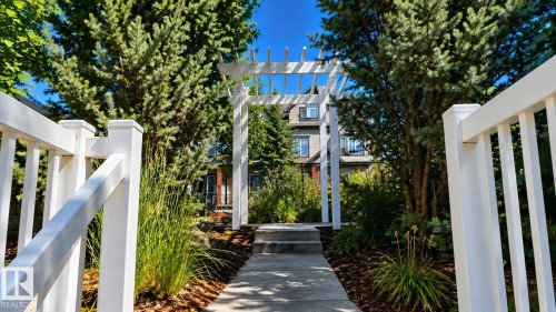 White pergola entryway with concrete pathway and steps, surrounded by established greenery and landscaping - #18 4850 Terwillegar Cm Nw, Edmonton, AB 
