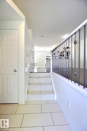 White panel door, staircase with tile treads, tile flooring, and metal baluster railing - #18 4850 Terwillegar Cm Nw, Edmonton, AB 