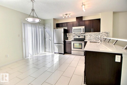 Kitchen featuring stainless steel appliances, dark wood-finish cabinetry, a patterned tile backsplash, and light-toned countertops - #18 4850 Terwillegar Cm Nw, Edmonton, AB 
