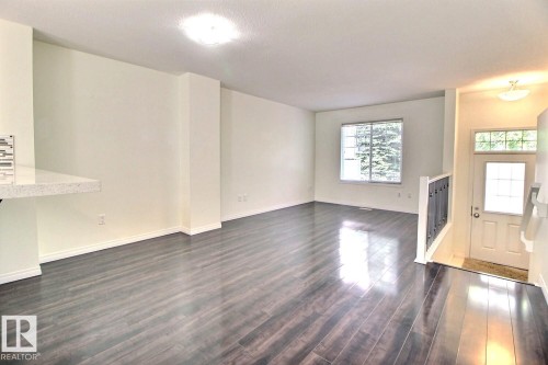 Spacious open area featuring wood-finish flooring, a contemporary window, and a built-in breakfast bar with a tile backsplash - #18 4850 Terwillegar Cm Nw, Edmonton, AB 