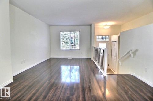 Spacious room featuring wood-finish flooring, white walls, and a large window - #18 4850 Terwillegar Cm Nw, Edmonton, AB 