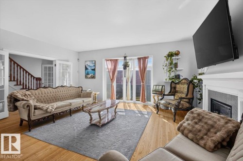 Light wood-finish flooring, white fireplace with tile surround, white trim, and a built-in staircase with wood railing - 17107 80 Avenue Nw, Edmonton, AB 