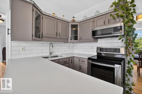 Kitchen featuring light gray cabinetry, white subway tile backsplash, light-toned countertops, and stainless steel appliances - 17107 80 Avenue Nw, Edmonton, AB 